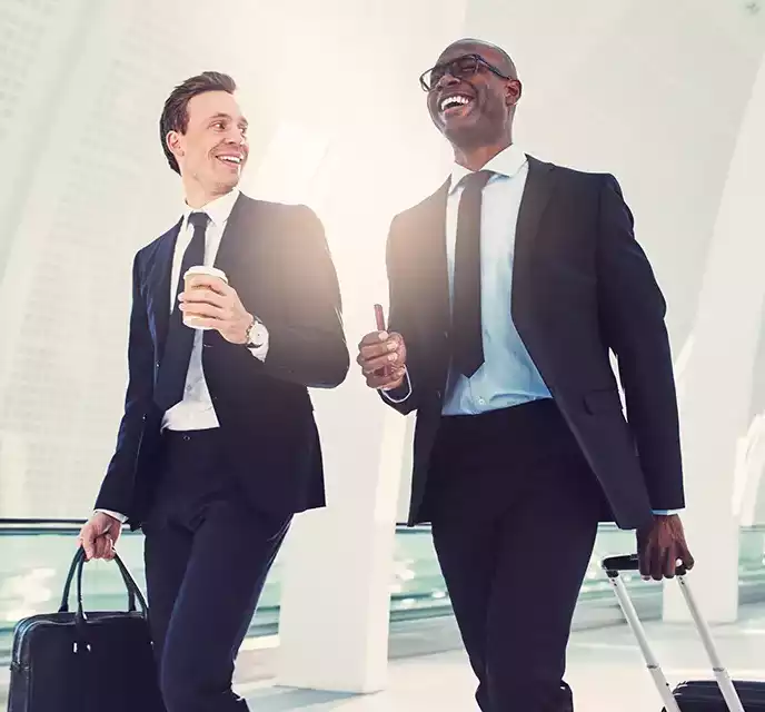 Two businessmen laughing together while walking through an airport terminal, representing a positive and enjoyable travel experience