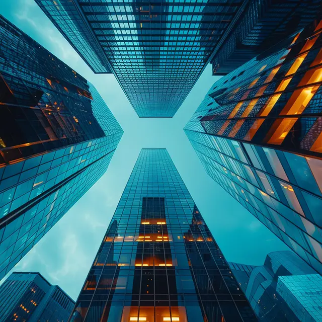 Skyward view of tall financial buildings illuminated in blue and orange hues, representing HYRYDE’s Global Chauffeur Network for seamless executive travel